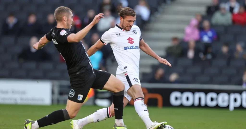 Alex Gilbey of Milton Keynes Dons attempts to move with the ball past Dean Campbell of Barrow AFC